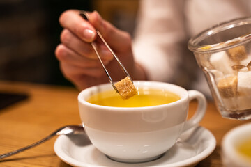 Close-up of a woman's hand throw brown sugar into a mug with tea.