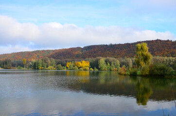 Indian summer at Lake Kratzmuehle in Altmuehltal valley in Bavaria, Germany, blue sky background, colorful fall foliage, reflections on water surface, a sunny day