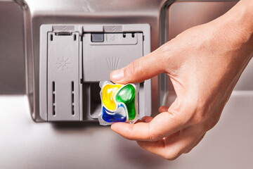 A tablet of a detergent for washing dishes in dishwashing machine in female hand.