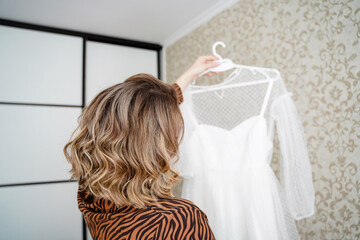 Pretty bride holding delicate white wedding dress on a hanger.
