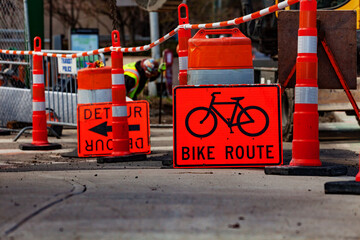 Orange street sign showing bike route detour during outdoor road construction works