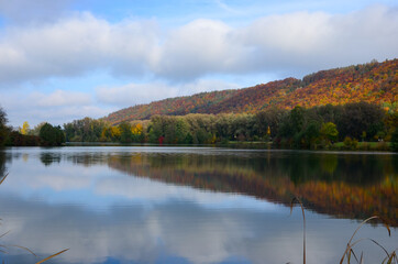 Indian summer at Lake Kratzmuehle in Altmuehltal valley in Bavaria, Germany, blue sky background, colorful fall foliage, reflections on water surface, a sunny day