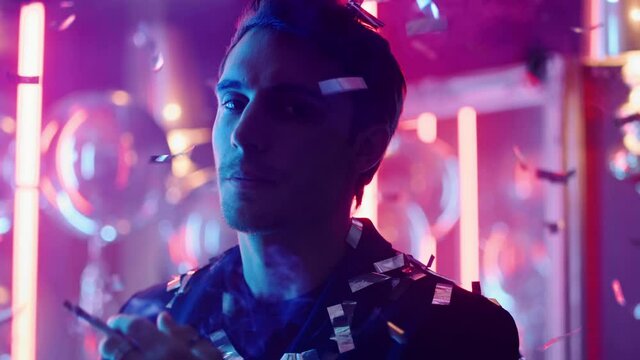 Young man smoking under confetti at party. Guy blowing smoke in nightclub