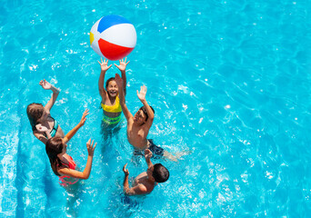 Group of kids in swimming pool play with inflatable ball view from above reaching hands up - obrazy, fototapety, plakaty