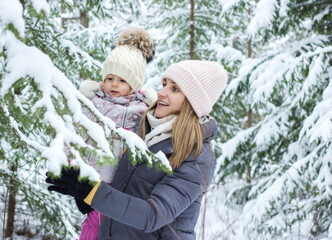 Fototapeta na wymiar Little girl with mother walking in snowy forest in winter.