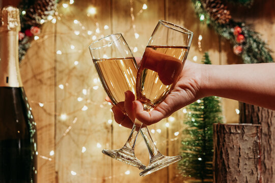 Two glasses of champagne in one hand on the background of Christmas decorations. The side with candles in a wooden candle holder. Image with selective focus and tinting.