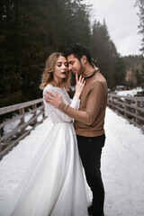 groom kisses bride winter standing on the wooden bridge. snowy forest park at sunny day