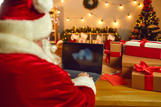 View From The Back Of Santa Claus Sitting At A Table And Turning On A Laptop For Work.