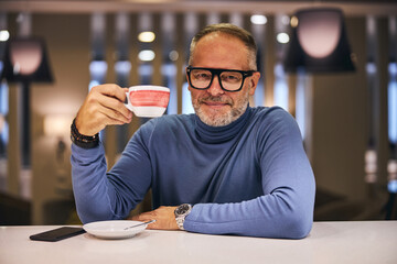 Smiling man with a lifted cup of coffee looking ahead