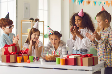 Little birthday girl blows out candles on a cake to the applause of her international friends.