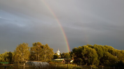 Rainbow in the sky, trees and a church below