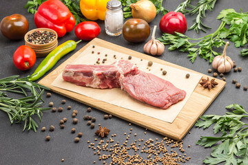 Veal meat with bone on cutting board. Set of vegetables and spices