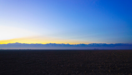 Obraz premium photograph of dawn over a plowed field against a background of mountains.