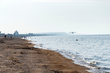 A small plane flies over the sandy seashore.