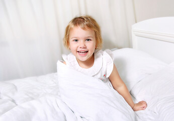 Child girl in bed smiling face..Toddler morning wake up.Caucasian little kid portrait.