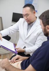 Obraz premium Young handsome man in beauty salon consults with beautician on anti-aging treatments. Doctor writing notes on clipboard and explain procedures to the patient