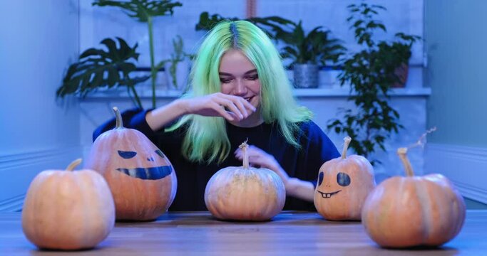 Halloween party, teenage girl with witch makeup sitting at the table with festive decorative pumpkins