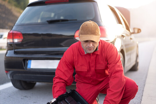 Handsome auto mechanic or road assistance worker in uniform repairing engine of the broken car on the road