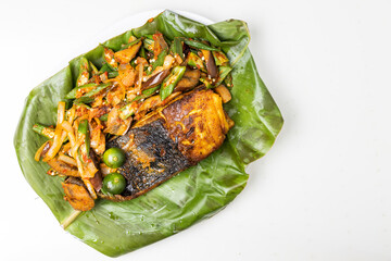 Overhead view of popular grilled stingray fish with spices and vegetable served on banana leaf