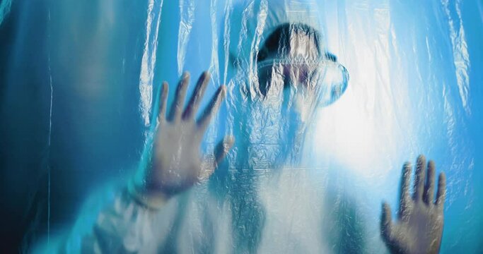 Medico o infermiere con tuta bianco covid si mette le mani in testa dalla disperazione dietro a un telo di plastica trasparente in ospedale.