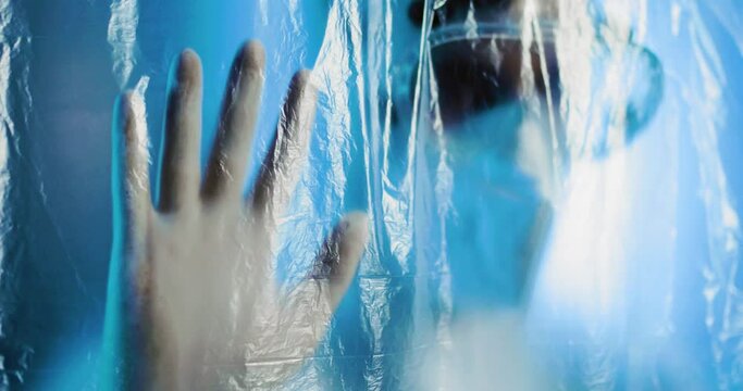 Medico o infermiere con tuta bianco covid si mette le mani in testa dalla disperazione dietro a un telo di plastica trasparente in ospedale.