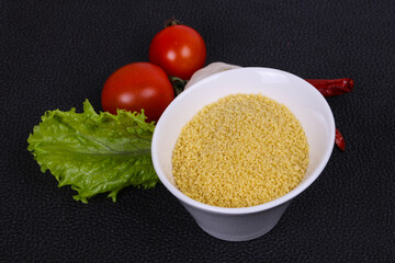 Raw couscous in the bowl served salad leaves, tomato and pepper