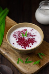Bubur Mutiara Merah Putih or Sago pearls porridge, Indonesian popular traditional dessert made from sago pearls and coconut milk, served on ceramic bowl, garnished with pandan leaves.