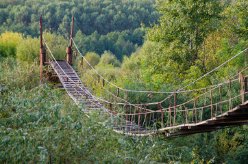Old wooden suspension bridge over a river in the wilderness.