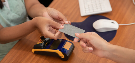 Close up of woman hands giving credit or debit bank card to cashier for checkout. Retail and payments concept