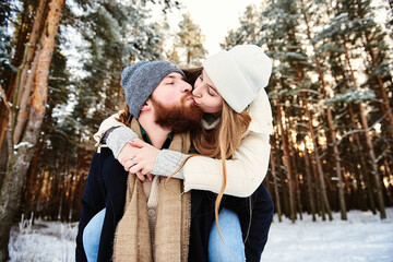 Happy kissing couple. Man giving woman piggyback ride on winter vacation in snowy forest