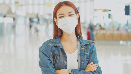 Young Asian woman passenger wearing medical face mask in casual clothes to prevent coronavirus at airport terminal. new normal travel and social distancing concept