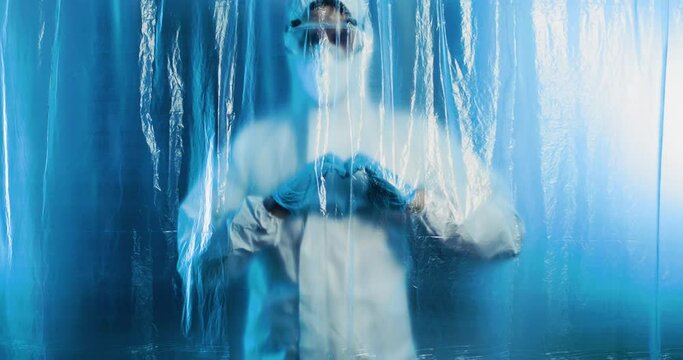 Medico o infermiere con tuta covid fa il simbolo del cuore dietro a un telo di plastica