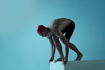 Professional caucasian male swimmer with hat and goggles practicing and training isolated on blue neoned studio background. Grace of motion and action. Healthy lifestyle, sport and movement concept.