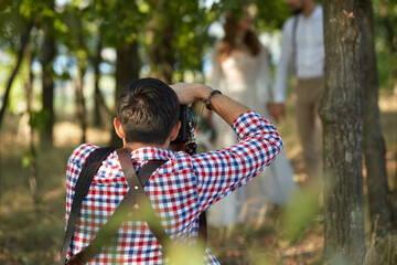 wedding professional photographer takes pictures of the bride and groom in park in sunny day, man photographer in action