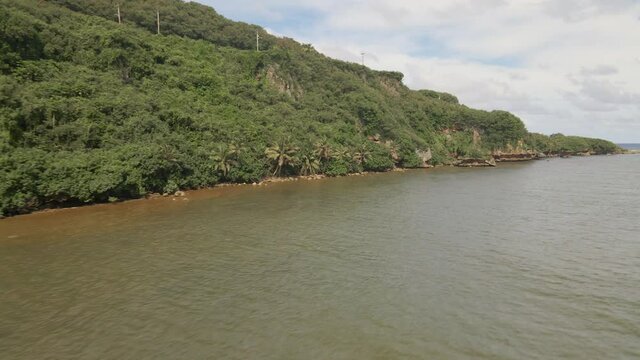 Drone flying low over the water near cliffs of a tropical island