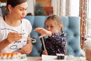 Mom with daughter eat sushi rolls in a cafe