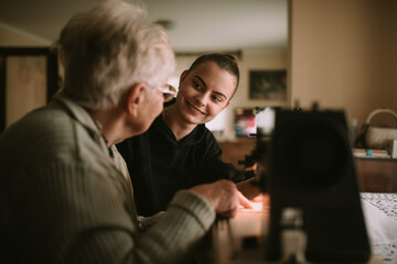 Senior sweet caucasian grandmother teaches her smiling teenage granddaughter to sew clothes on a sewing machine in her grandmother's house. The focus is on the teenage girl