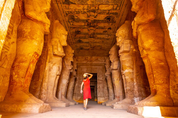 A young woman in red dress looking at the pharaohs at the Abu Simbel Temple in southern Egypt in...
