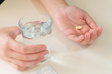 Yellow pill and a glass of water in female hands, on desk. health concept