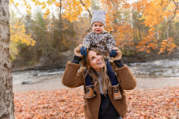 Little girl and her mother playing in the autumn park with child girl on shoulder