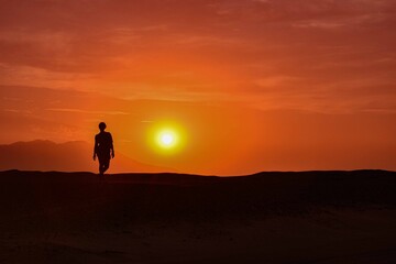 Fototapeta na wymiar silhouette of a person walking on the desert at sunset