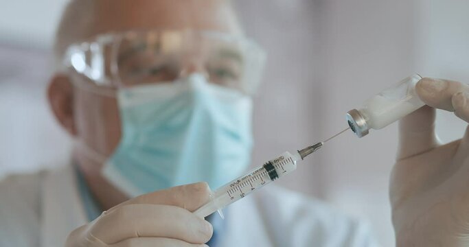 Close up shot of unrecognizable nurse or doctor in gloves filling syringe from ampule with covid-19 vaccine. Nurse filling injection syringe from vial.