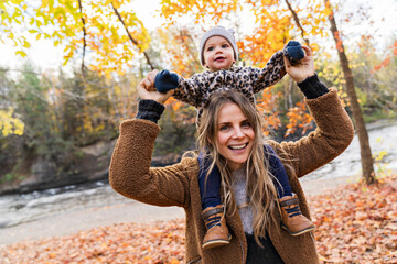 Little girl and her mother playing in the autumn park with child girl on shoulder