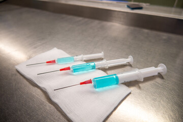 3 differently sized syringes filled with blue liquid lie on a white compress