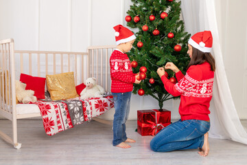 mother and child decorate the Christmas tree before the new year or Christmas in the children's room with a new year's interior