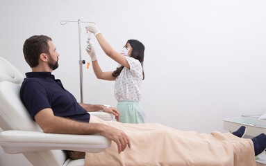 Nurse or doctor preparing and adjusting infusion for young man patient in hospital or beauty salon....