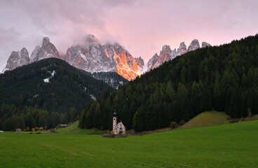 Abendrot über den schneebedeckten Geisler spitzen in den Südtiroler Dolomiten mit kleiner Kapelle