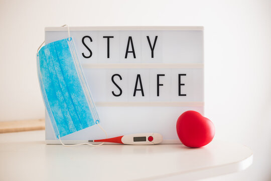 Lightbox sign with text hashtag #STAY SAFE  with a blue mask a red heart on a white desk COVID-19. Stay safe concept