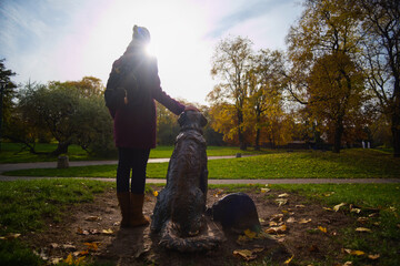 Młoda kobieta trzymająca rękę na pomniku psa w parku. 