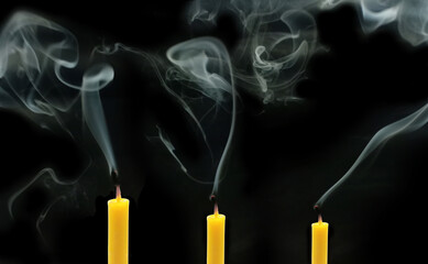 Three yellow candles that have been extinguished with smoke on black background.